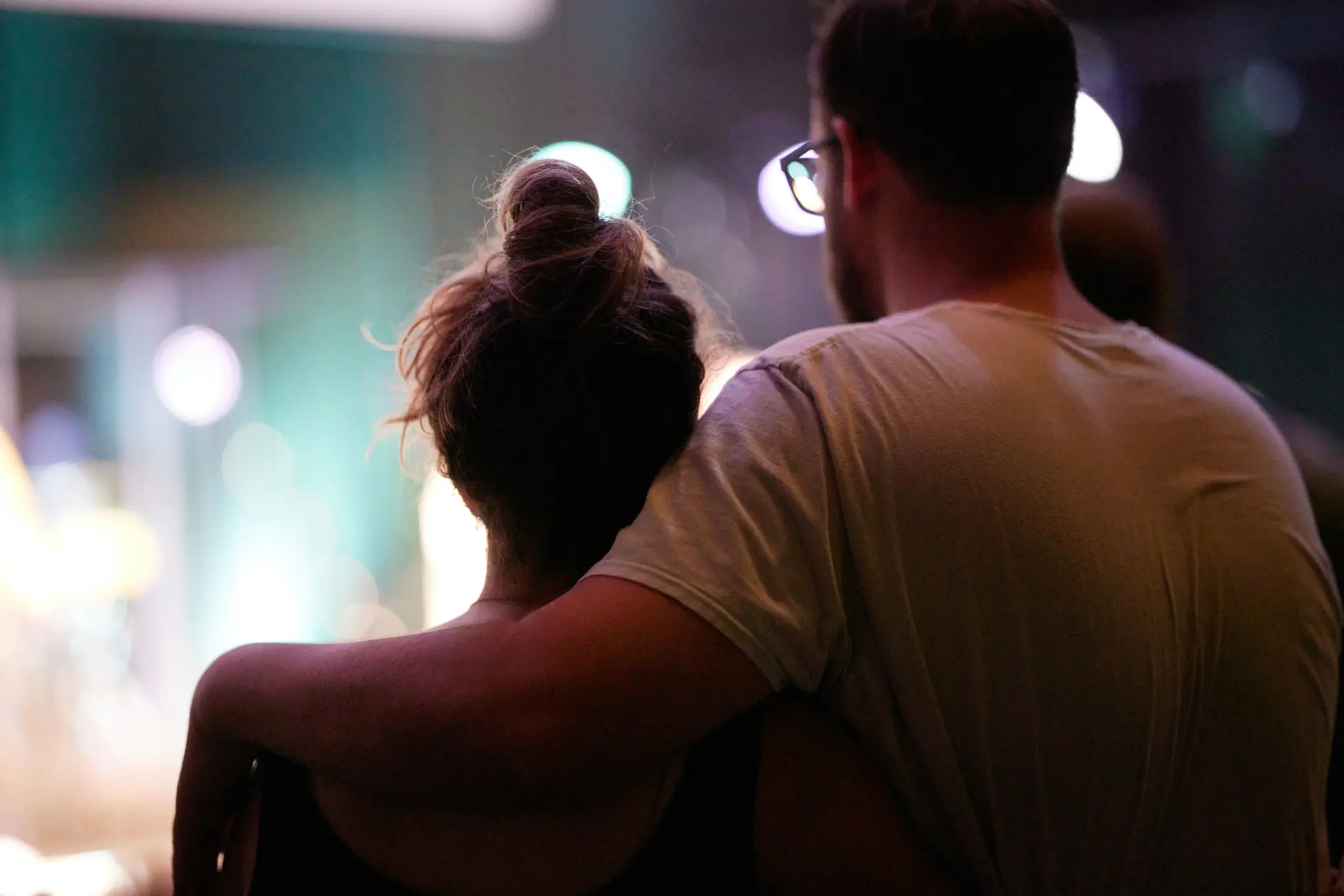 Couple sitting close together watching a stage with soft lighting.