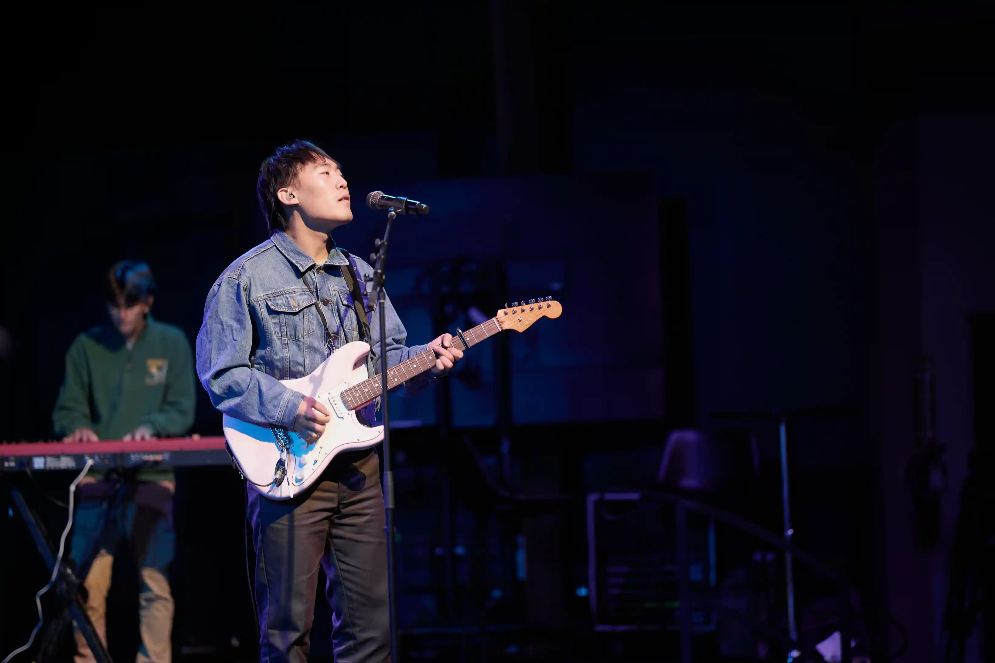 Musician playing electric guitar and singing on stage under spotlight.