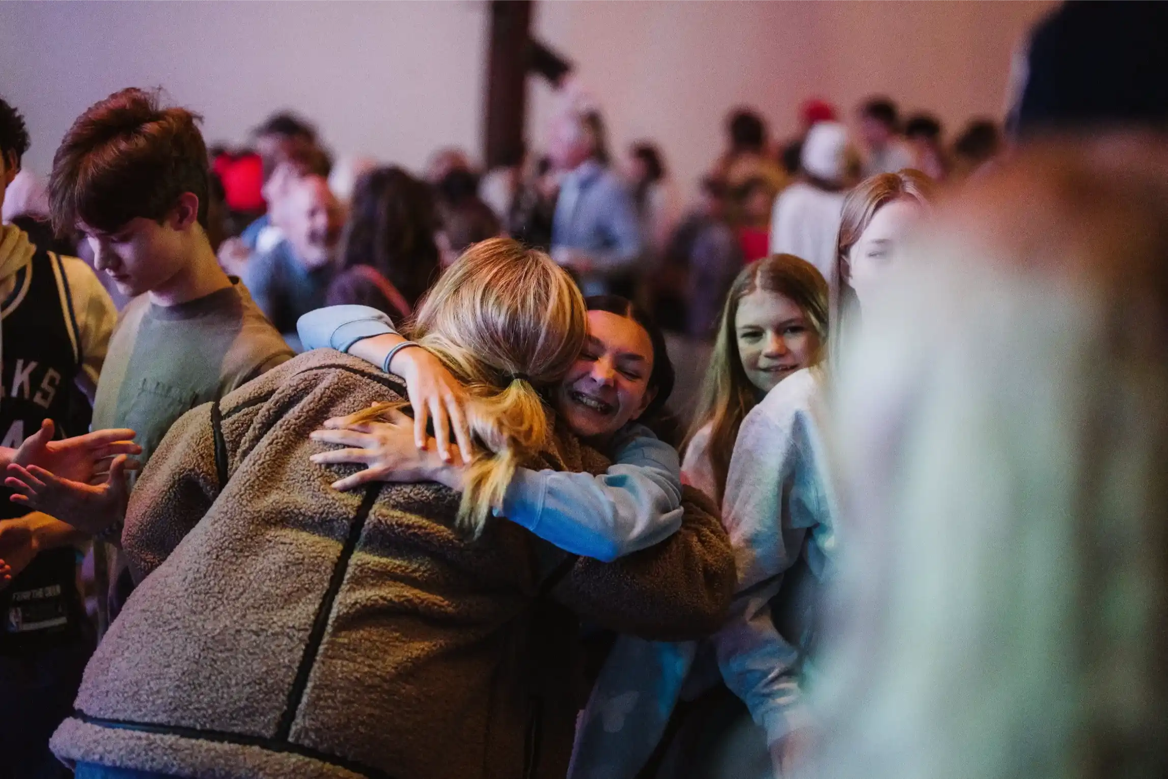 Friends hugging and smiling in a crowded indoor event.