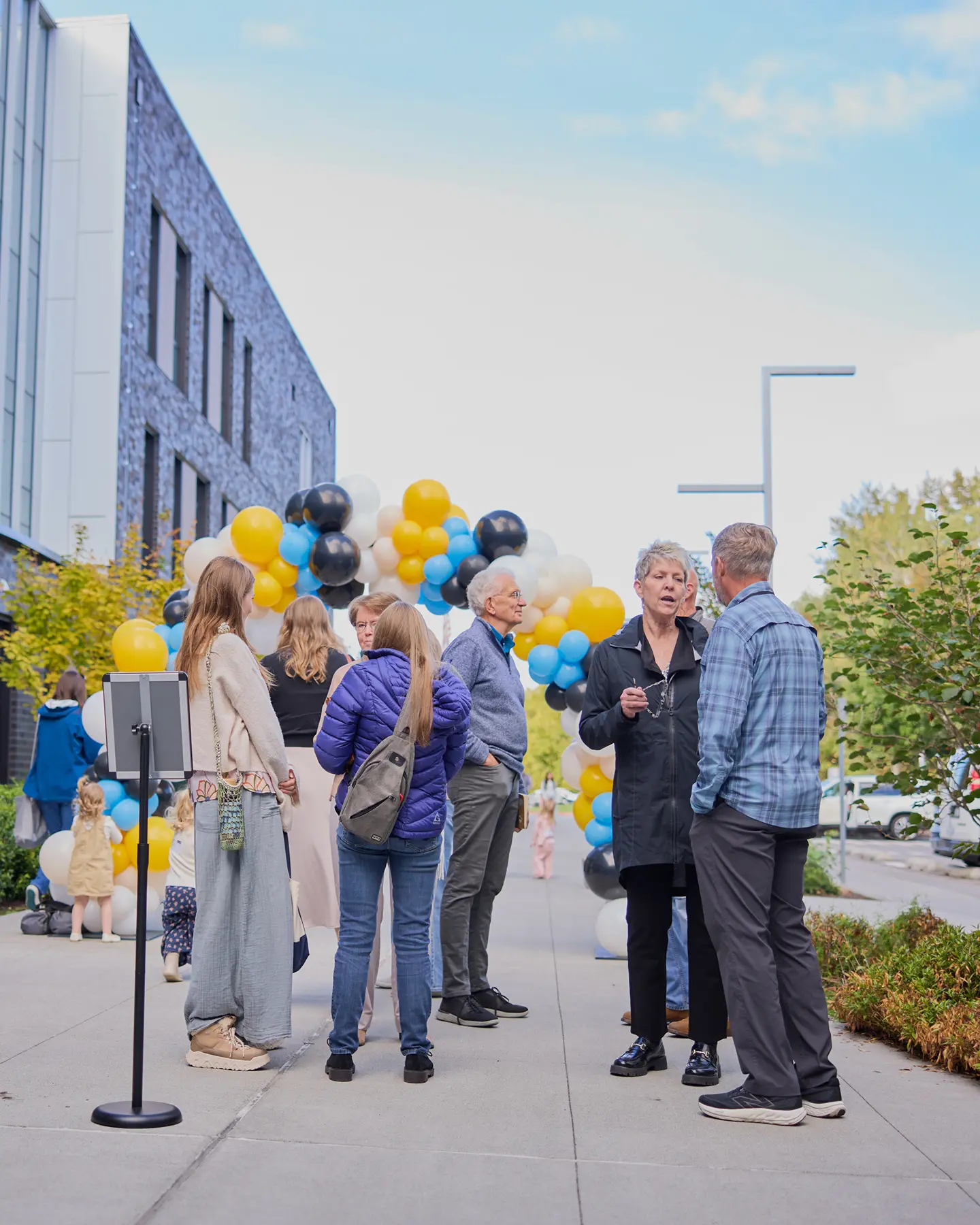 People socializing outdoors with colorful balloons near a modern building.