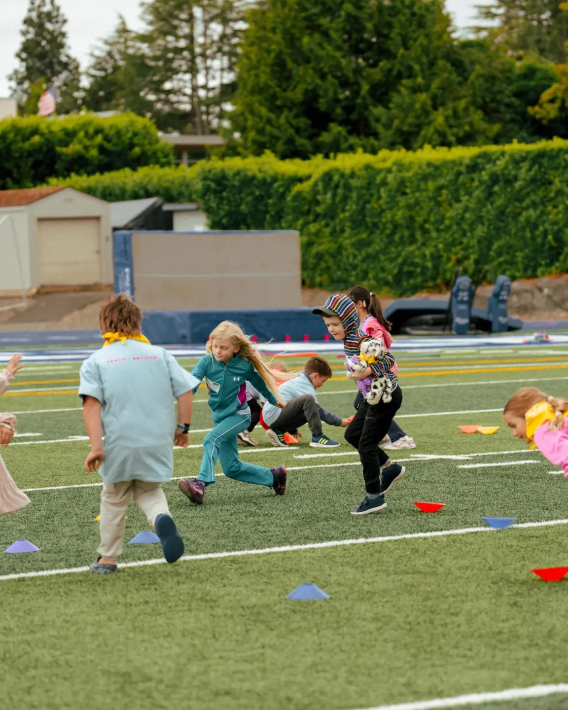 Group of children playing and running on a sports field marked with cones.
