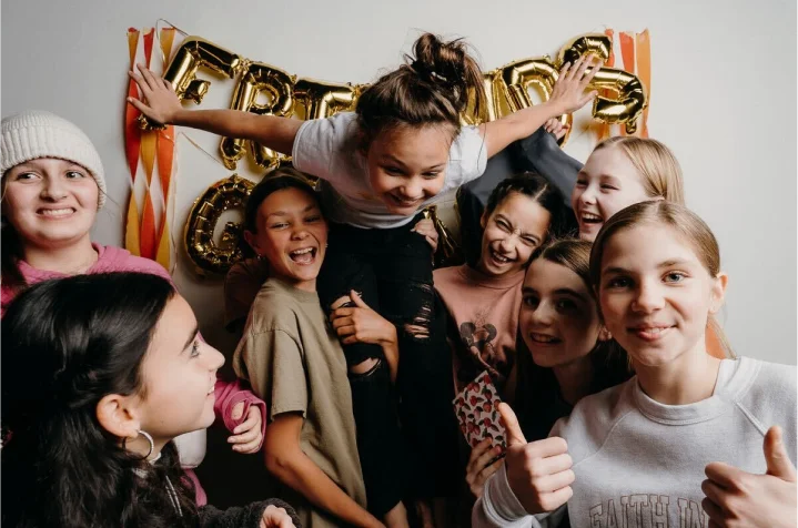 Group of smiling friends posing playfully in front of 'FRIENDS' gold balloon decorations.