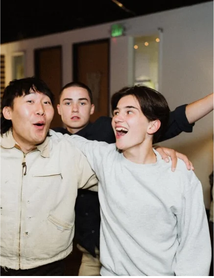 Three young friends indoors, with two smiling and one looking at camera.