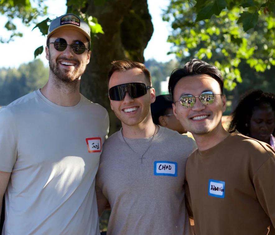 Three young men smiling outdoors wearing sunglasses and name tags labeled Jared, Chad, and Xiao Xiao.