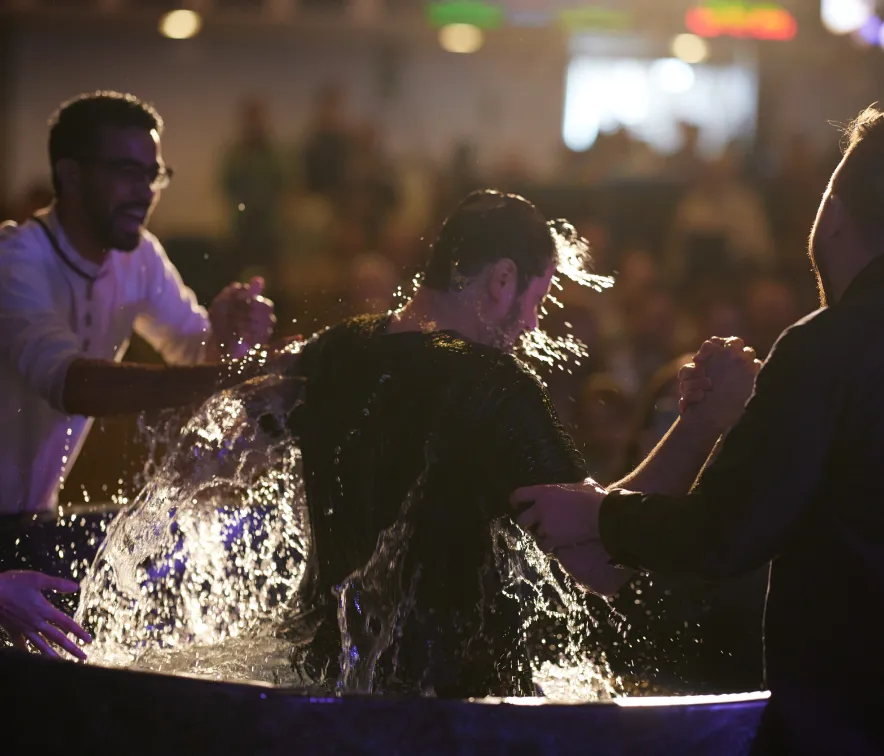 Man being baptized with water splashing as two men hold his hands during the ceremony.