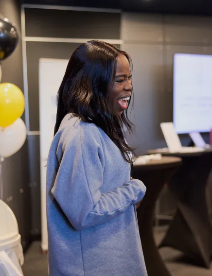 Smiling woman with long dark hair wearing a gray sweater at an indoor event.