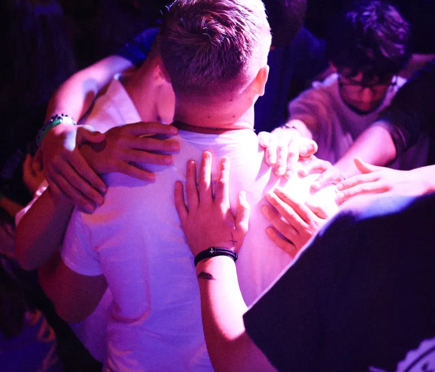 Group of people placing their hands on a person wearing a white shirt, illuminated by purple light.