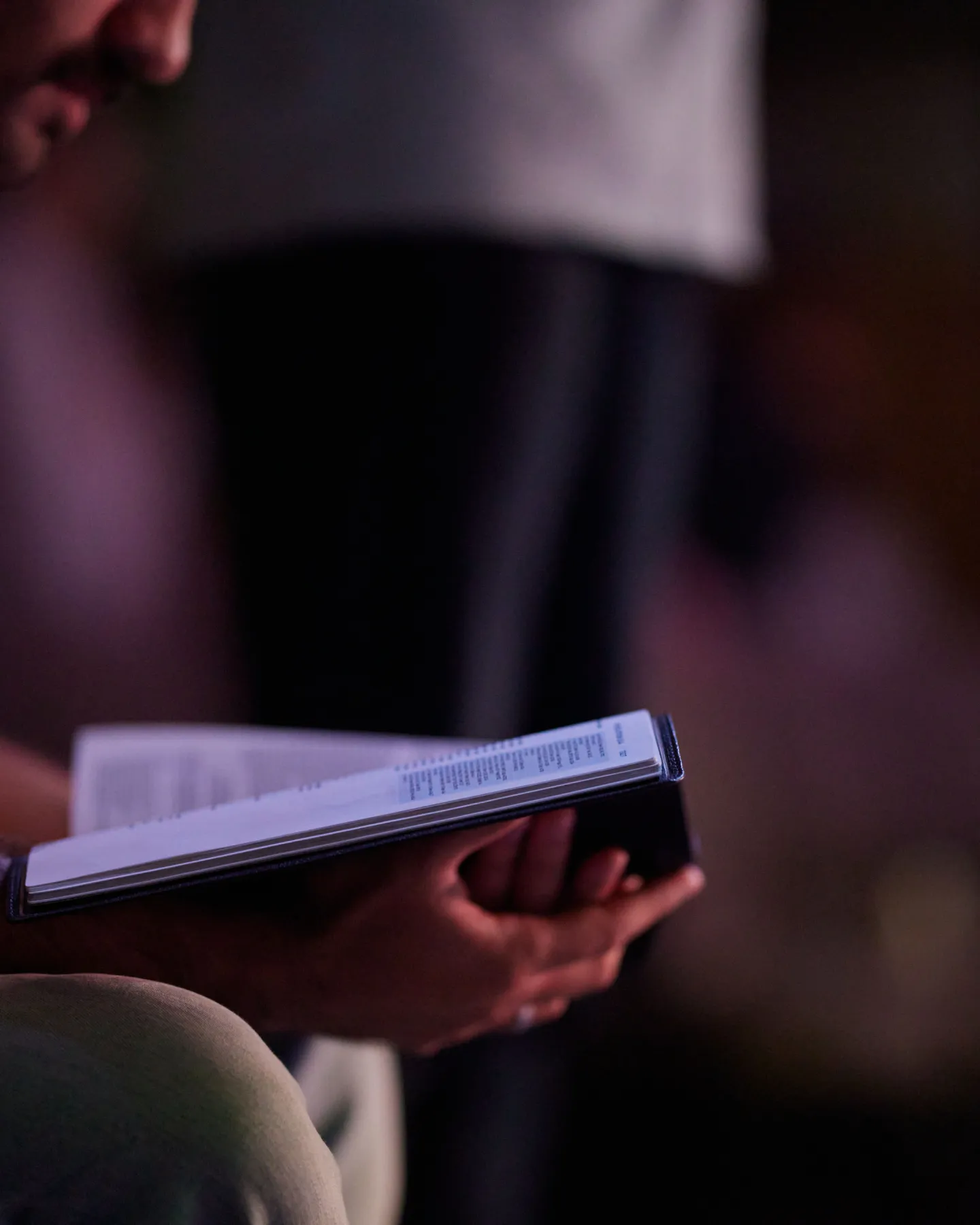 Person holding and reading an open book during a service, with dim lighting and blurred background.
