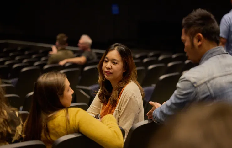 Three people conversing in a dark auditorium with rows of empty seats around them.