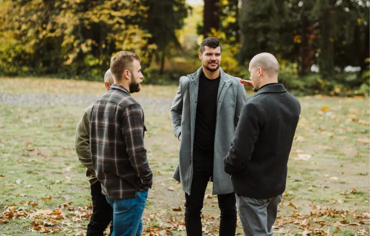 Four men standing and talking outdoors in a park with autumn leaves on the ground.