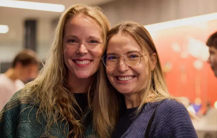 Two smiling women with long hair posing closely together indoors at a social event.