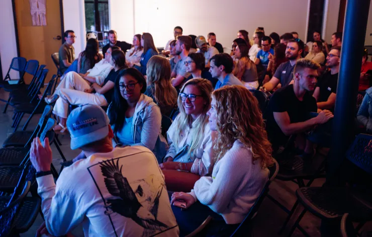 A diverse group of people seated in rows indoors, engaged and watching a presentation or event.