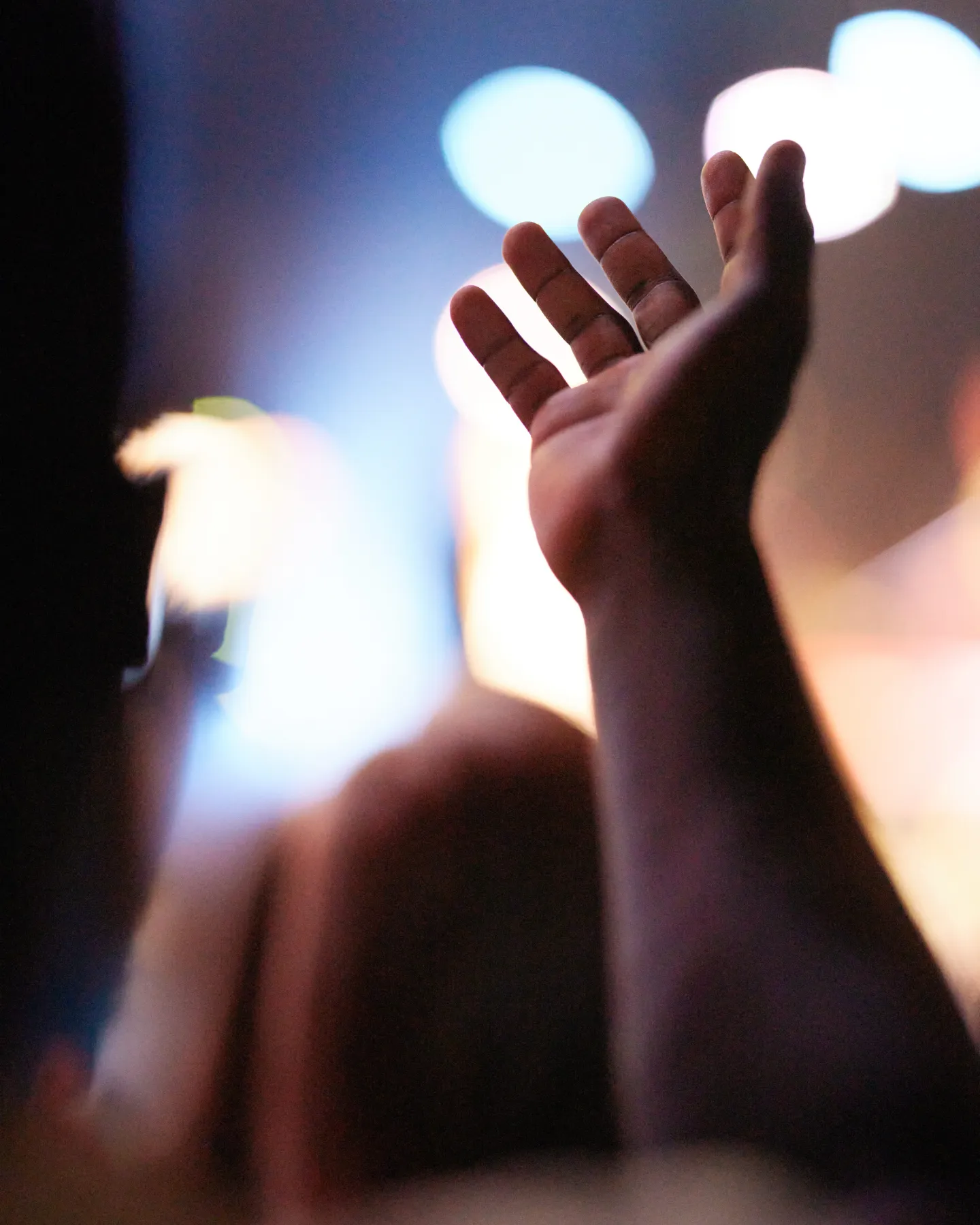 A raised hand with fingers spread, illuminated against a blurred background of lights.