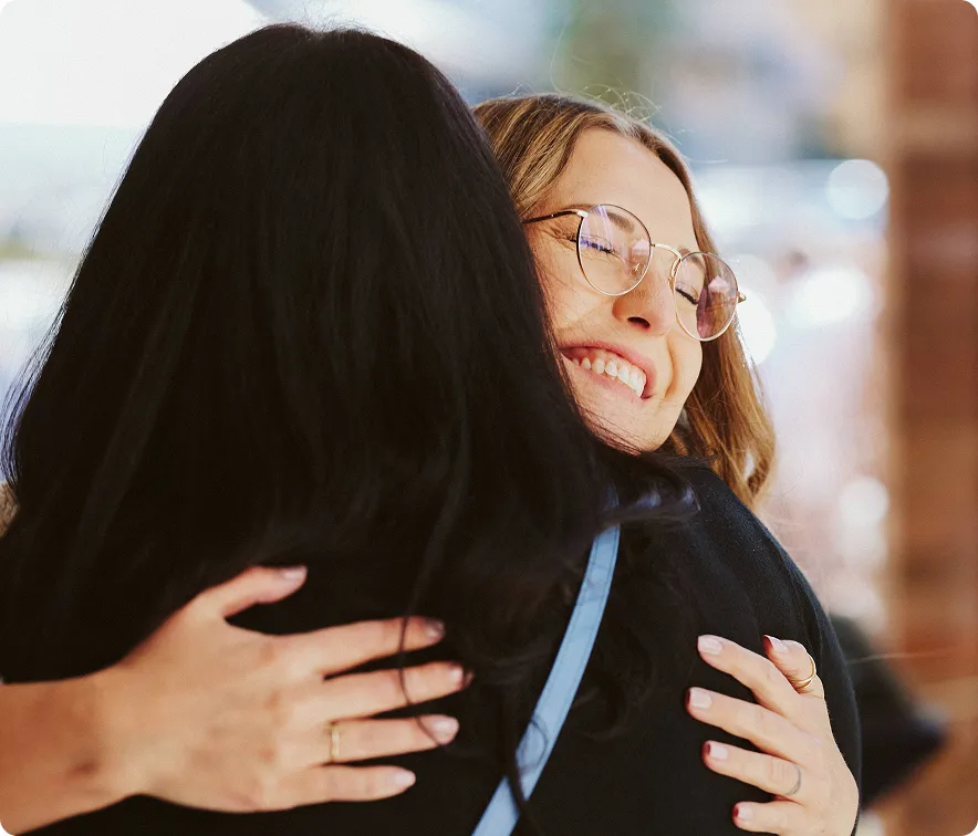 Two women embracing, one with glasses smiling with eyes closed.