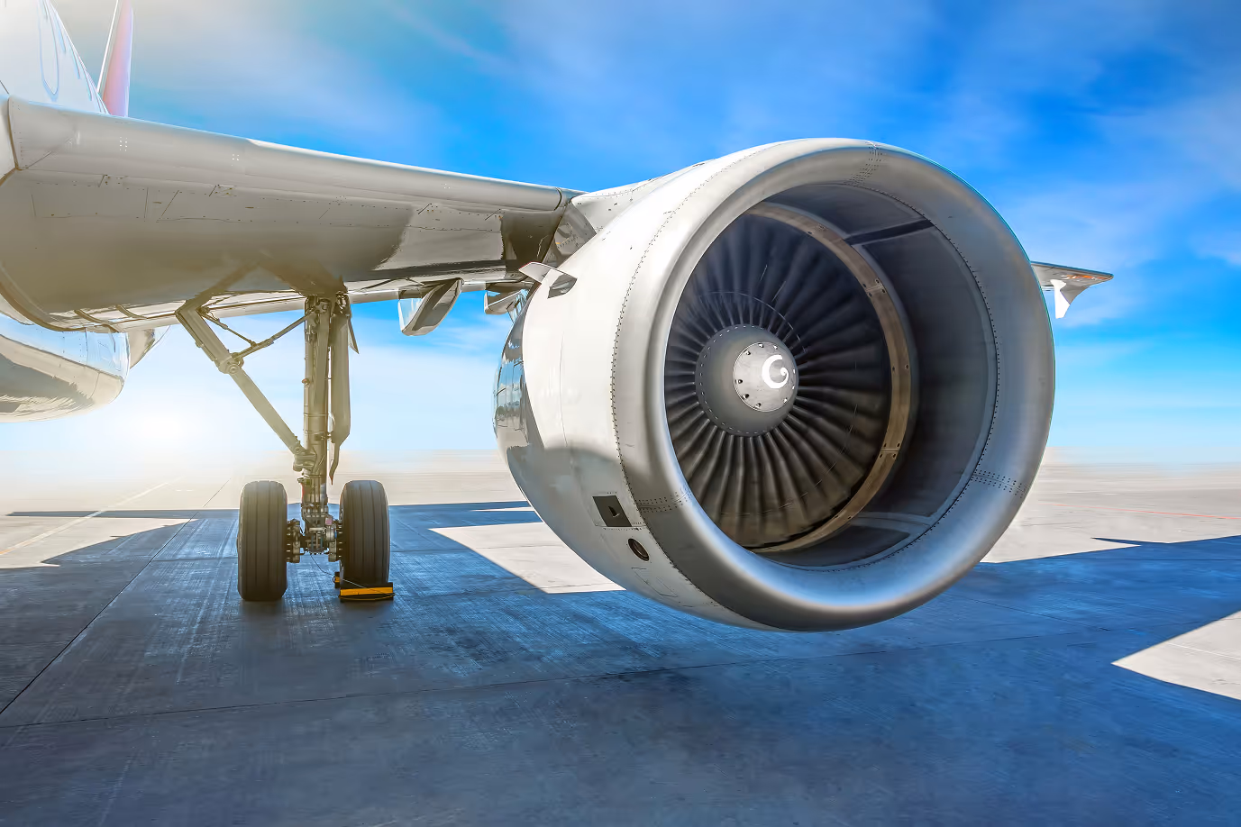 Close-up of an airplane jet engine and landing gear on a runway under a clear blue sky.