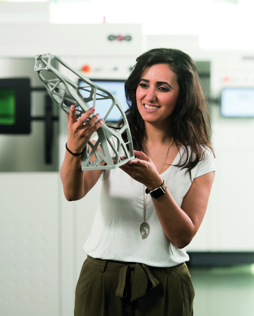 Natascha Jafari hält ein 3D gedrucktes Bauteil in den Händen hoch.