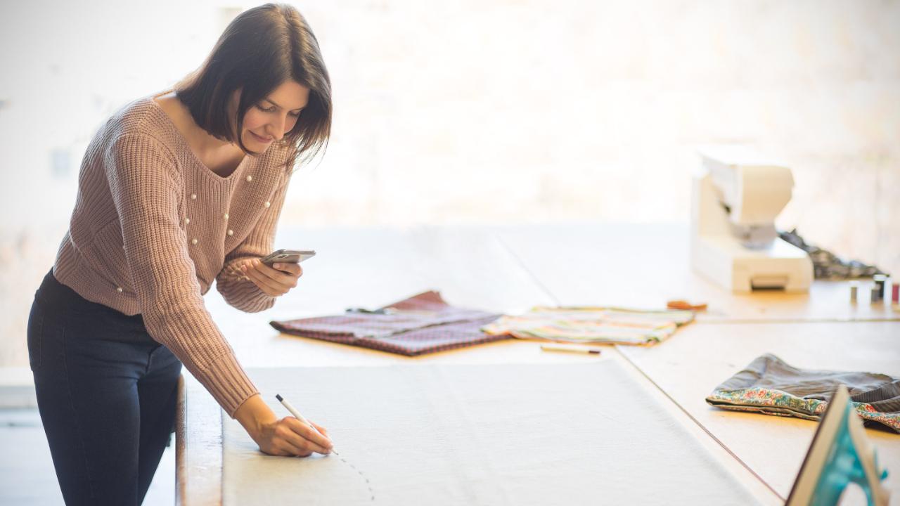 Frau markiert Stoff am Tisch und nutzt ein Smartphone als Referenz. 