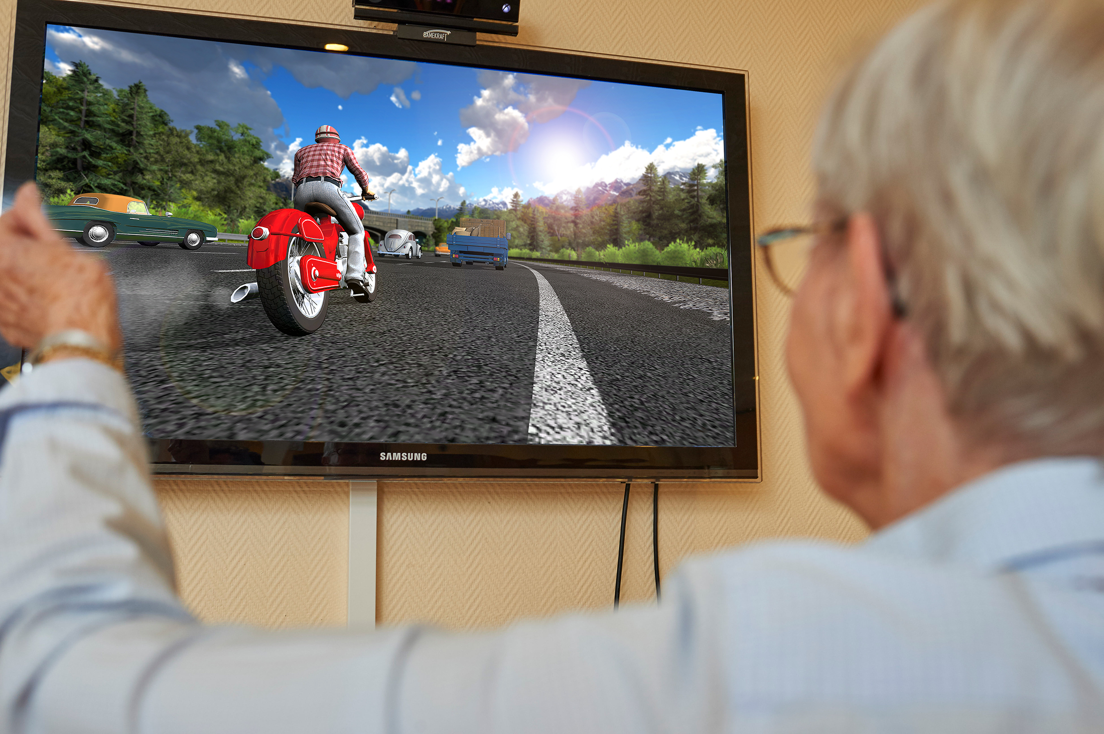Eine ältere Person spielt eine Motorrad-Fahrsimulation auf einem großen Fernsehbildschirm.