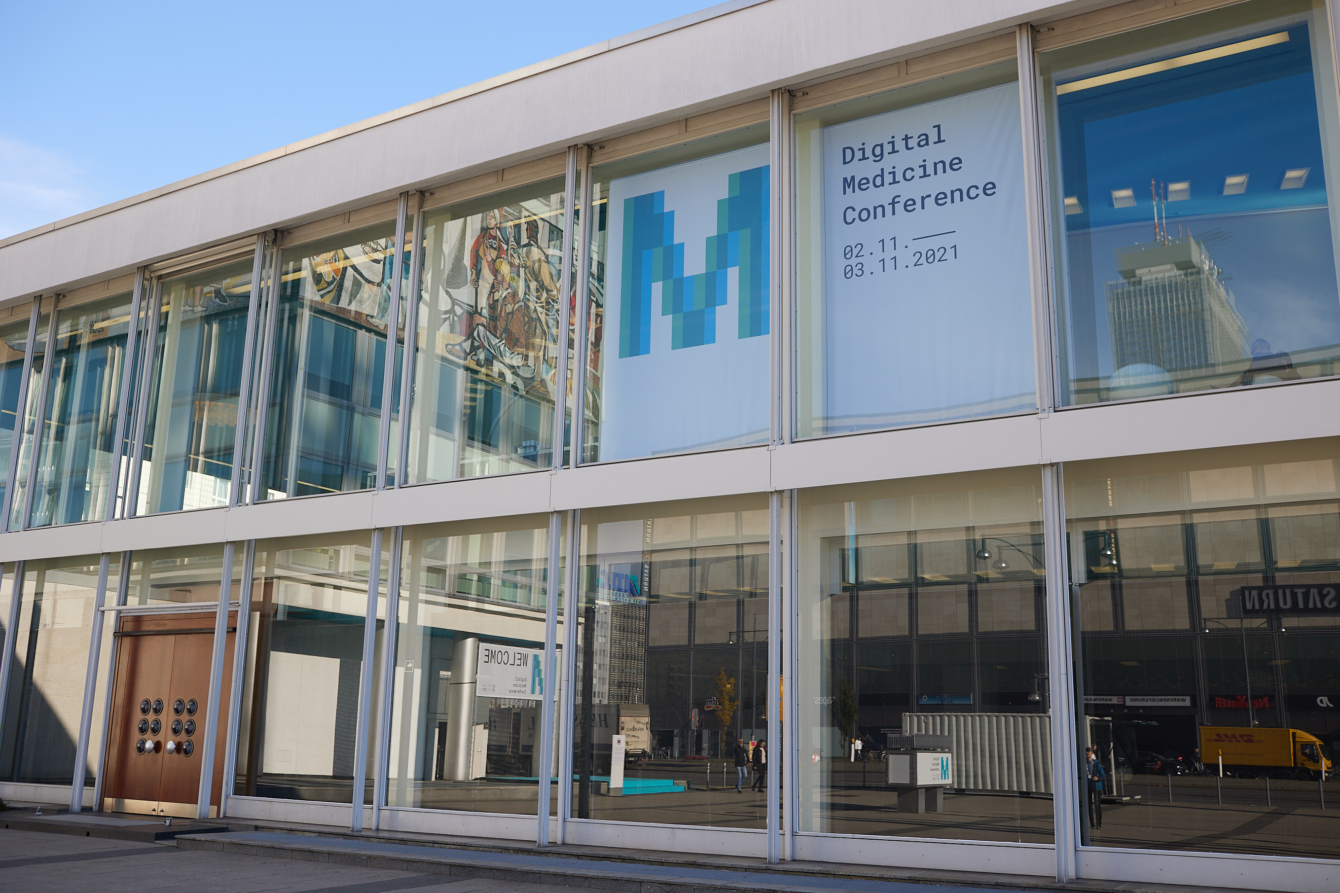 Zwei Plakate der Konferenz hängen an der Glasfassade des Gebäudes.