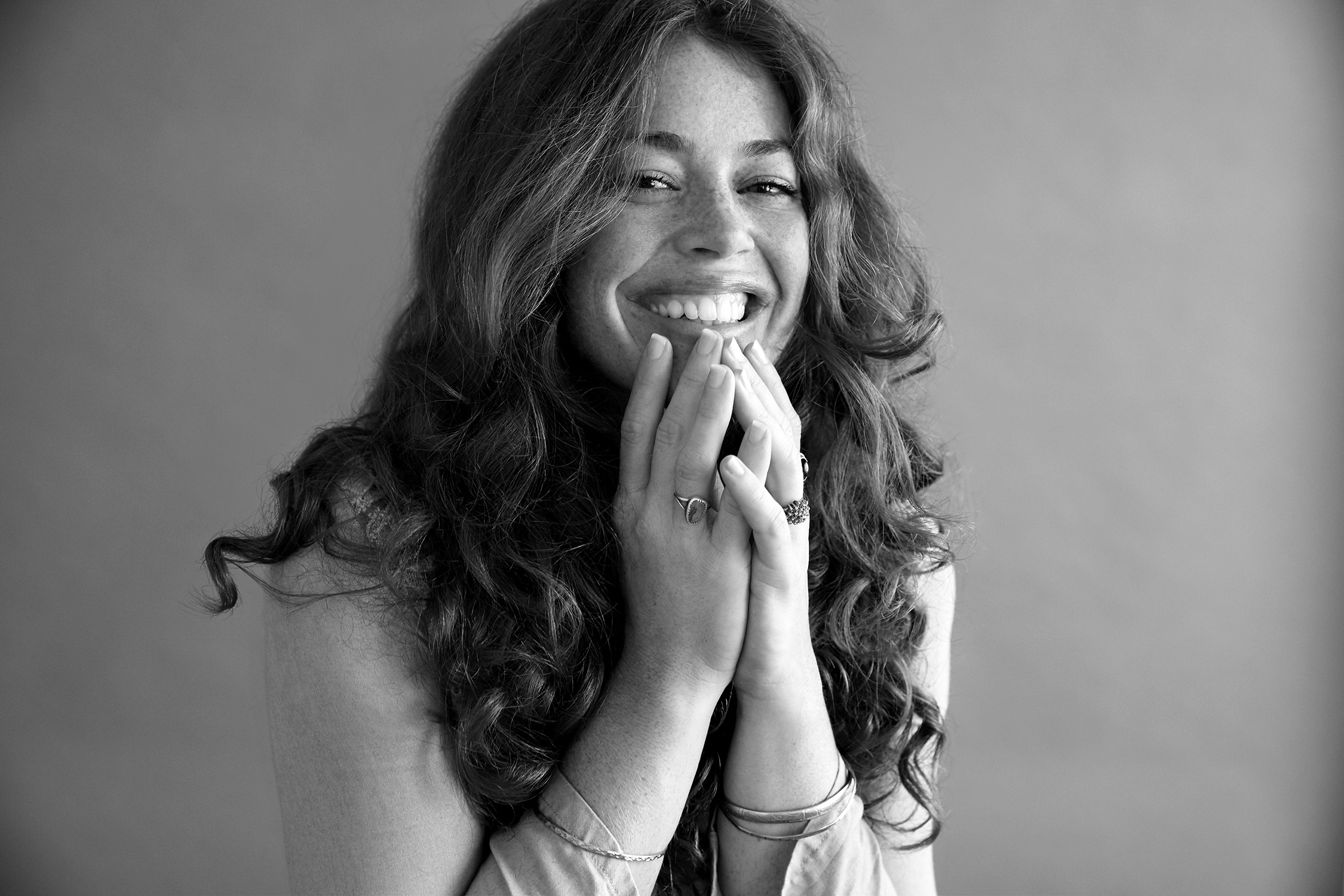 Smiling model with curls and freckles has her hands on her chin with a black-and-white filter.