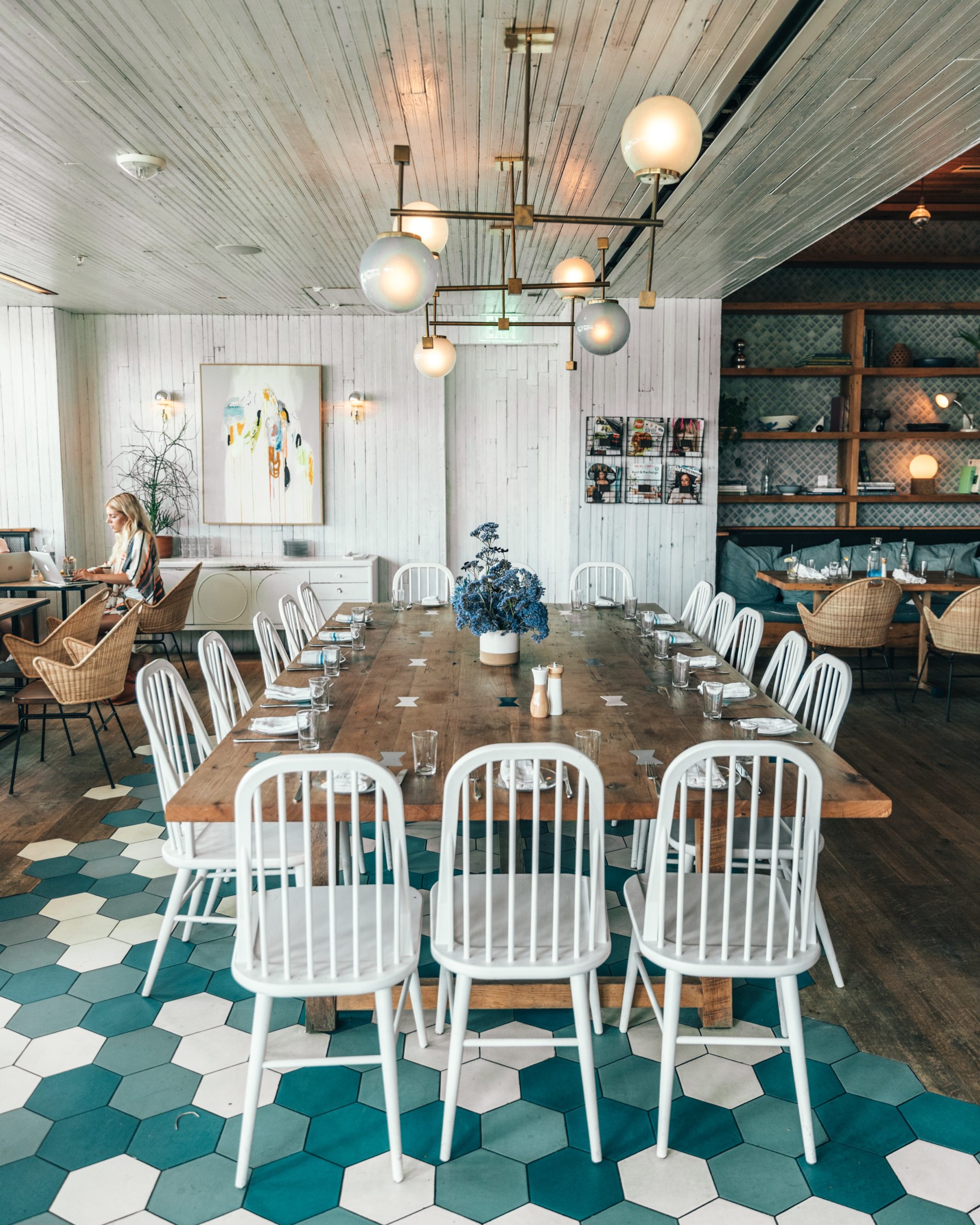 Restaurant mit langem Holztisch und weißen Stühlen.