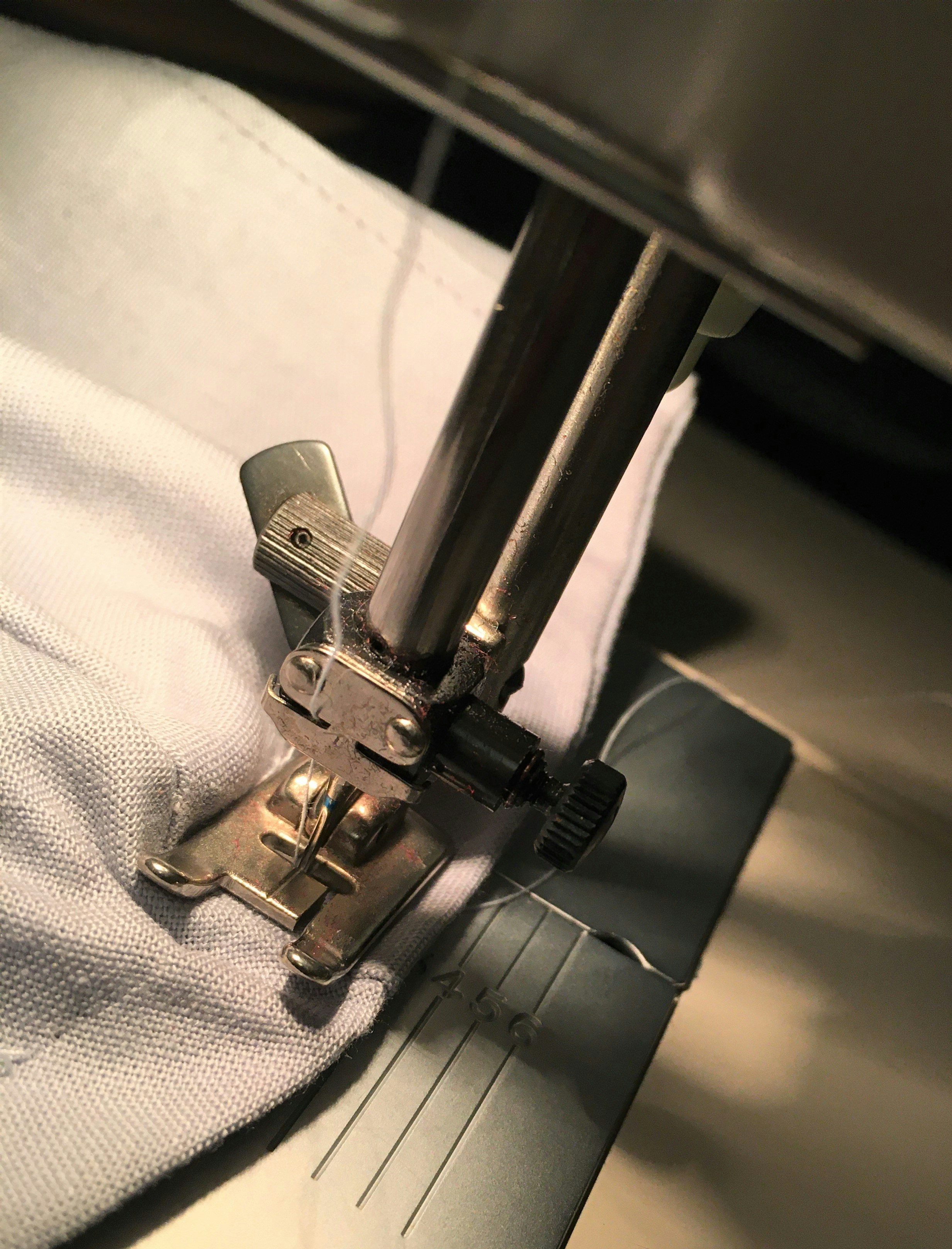 Nähmaschine näht helles Textil in Detailansicht.