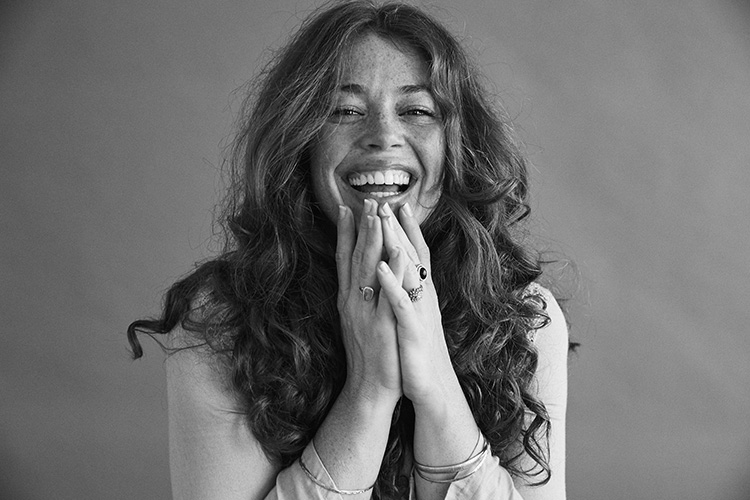 Smiling model with curls and freckles has her hands on her chin with a black-and-white filter in the foreground.