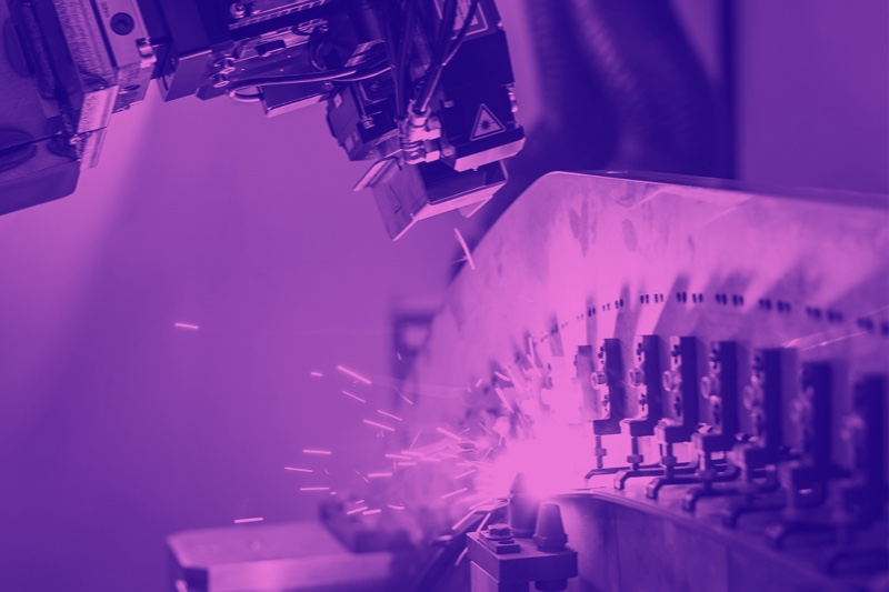 Industrieroboter bei der Metallbearbeitung mit Funkenflug in violetten Farbfilter.