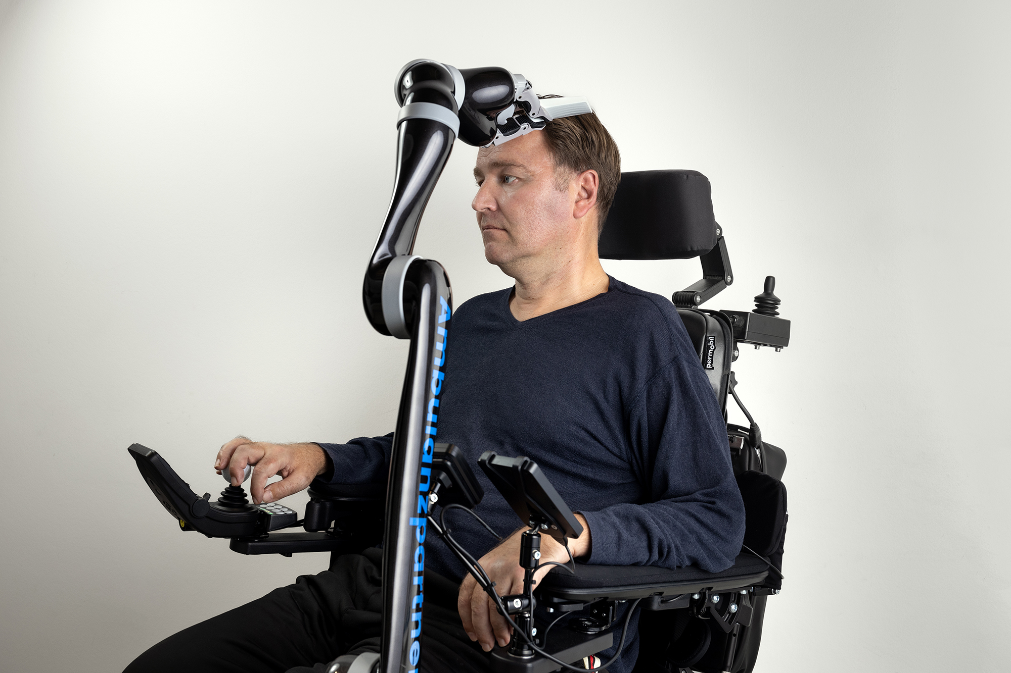 Mann im Rollstuhl wird von einem Roboterarm gekämmt.