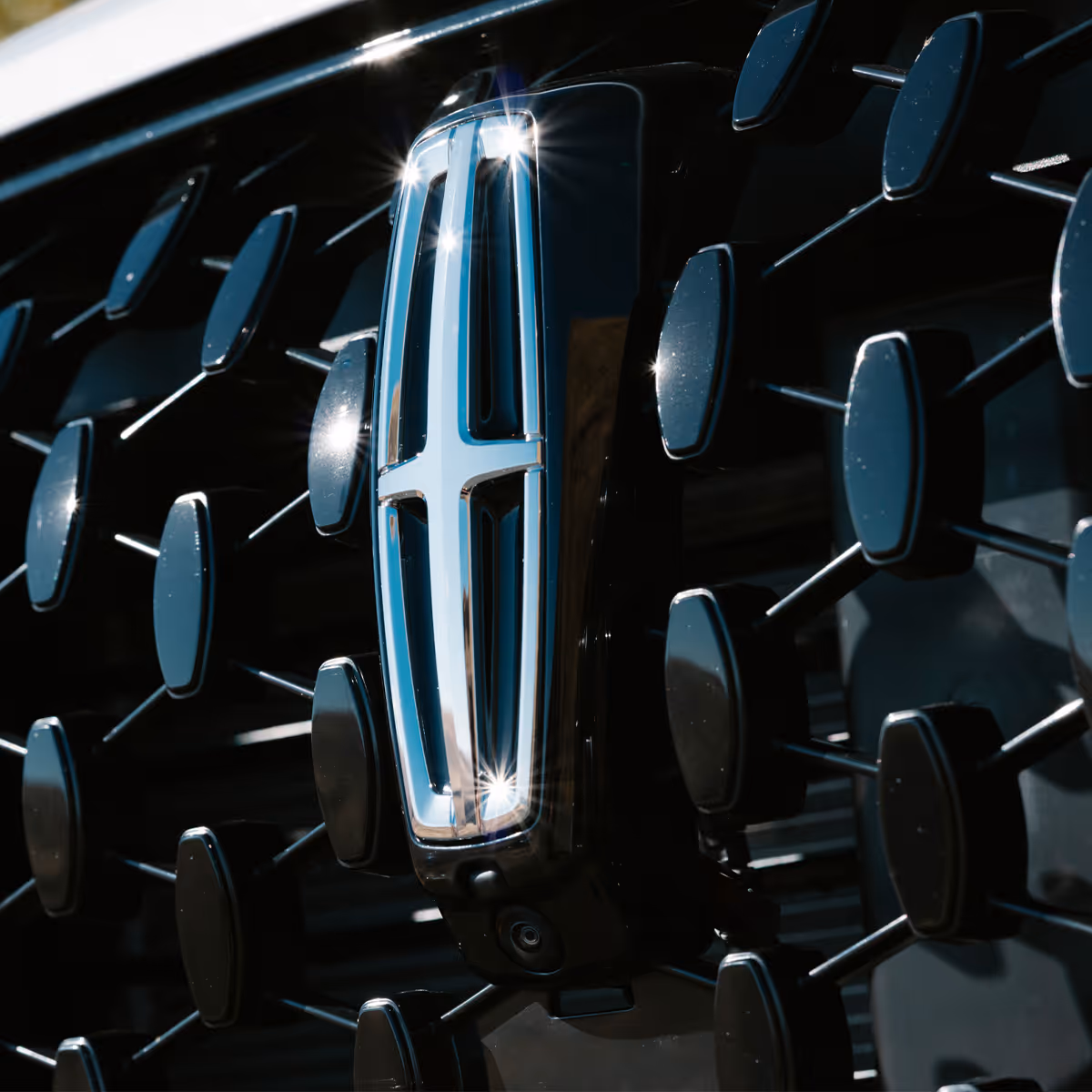 Close-up of a chrome Lincoln star logo centered on a dark textured front grille with geometric fin details.