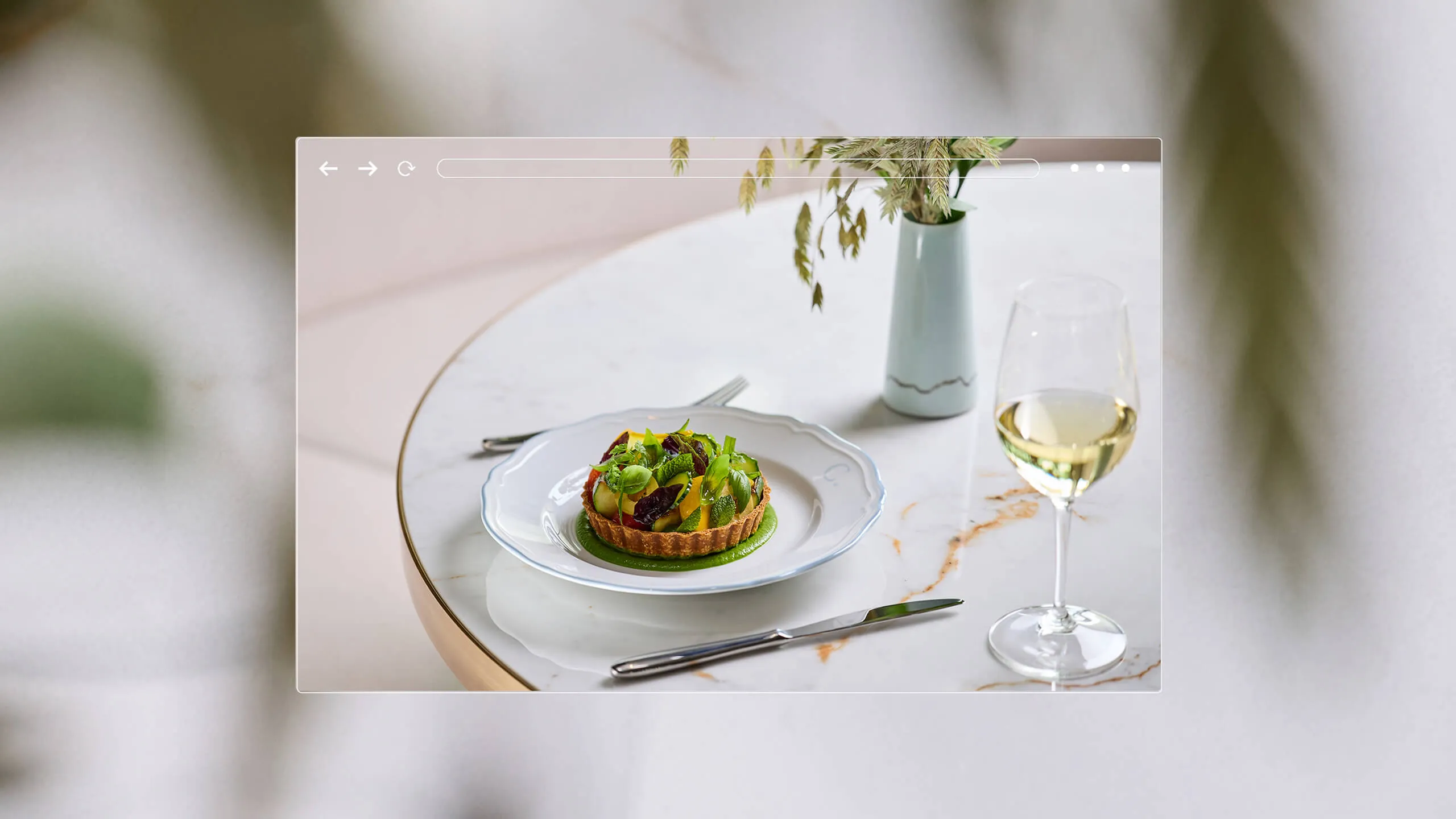 Gourmet vegetable tart on a white plate with green sauce, set on a marble table with a glass of white wine and a vase with dried plants.