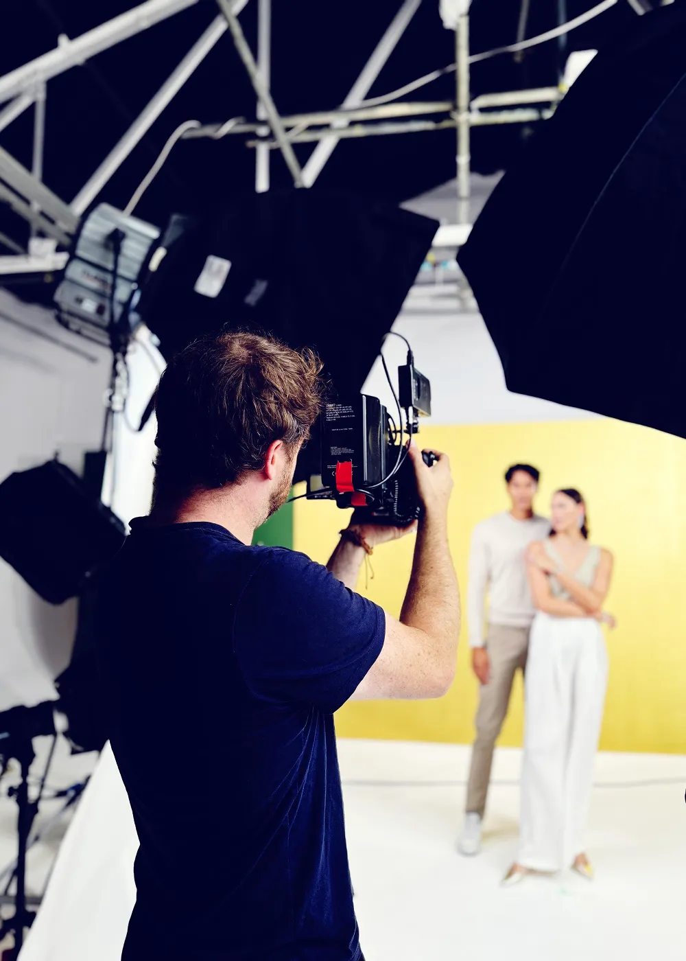 Photographer filming a couple posing in a bright studio with professional lighting equipment.