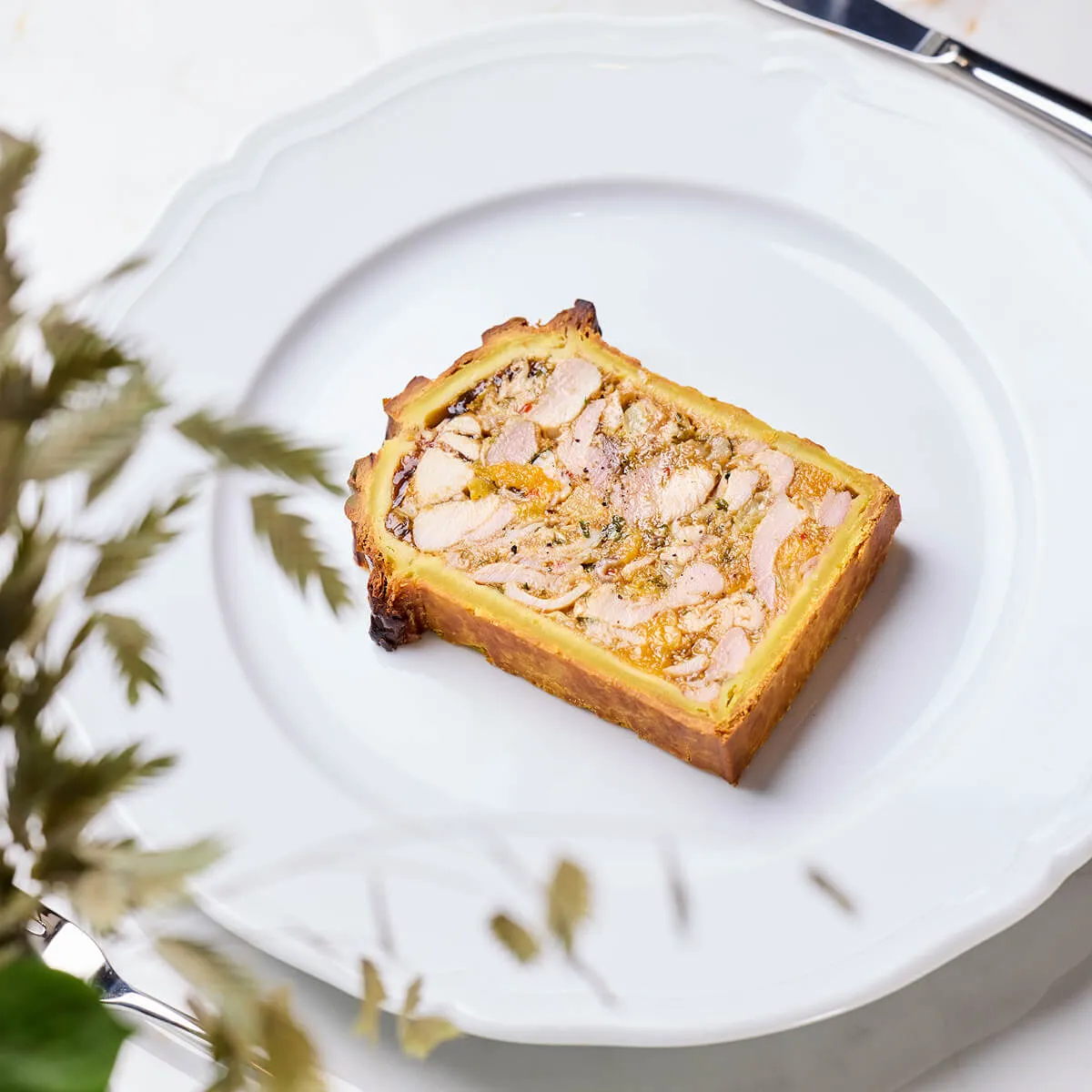 Rectangular slice of savory meat terrine on a white plate with a scalloped edge.