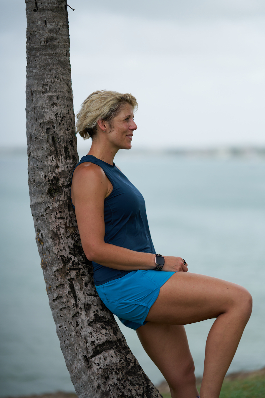 Ruth Mac leaning against a palm tree with the sea in the background.
