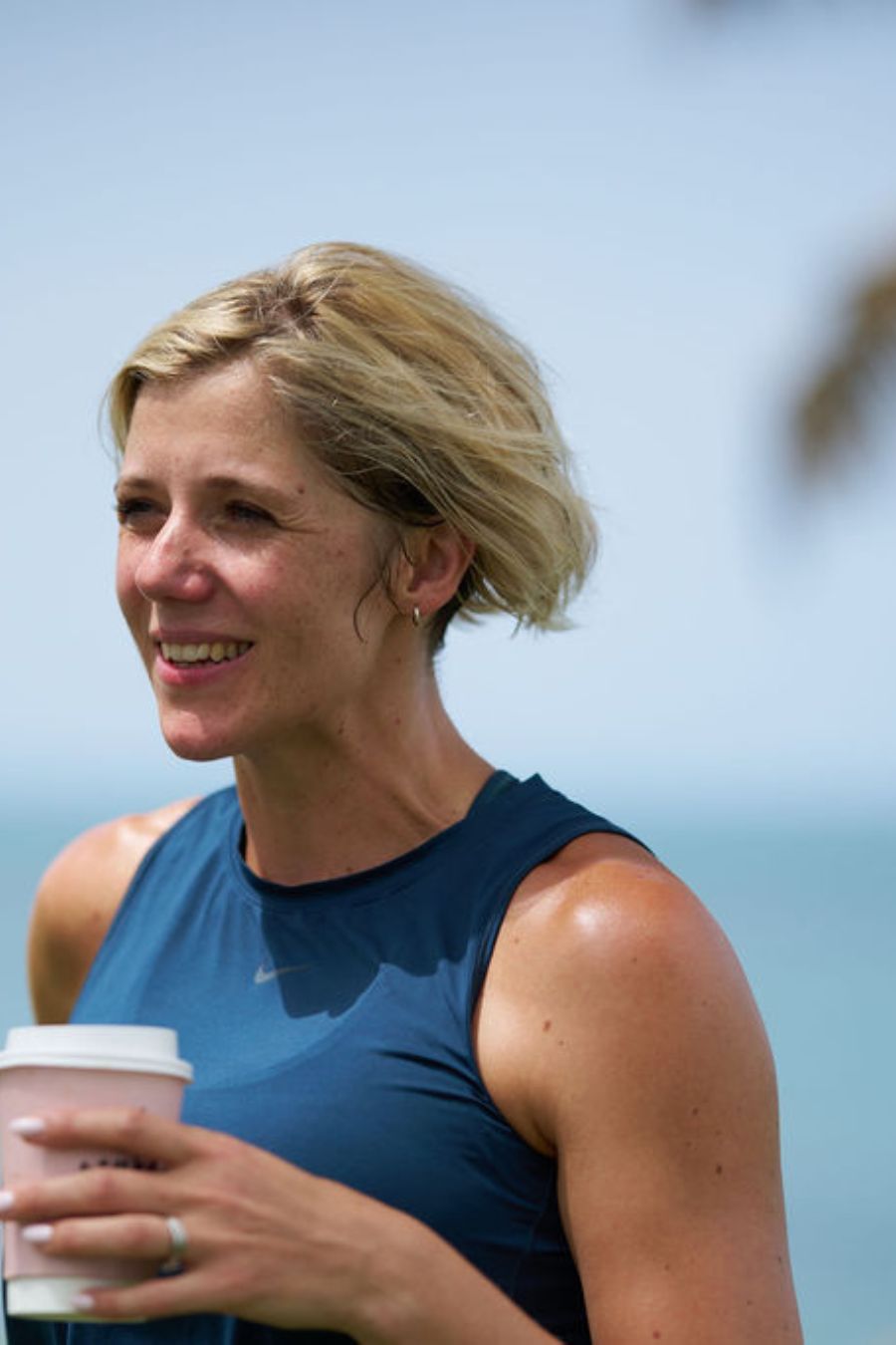 Ruth Mac holding a hot drink in a cardboard cup, with the sea in the background.