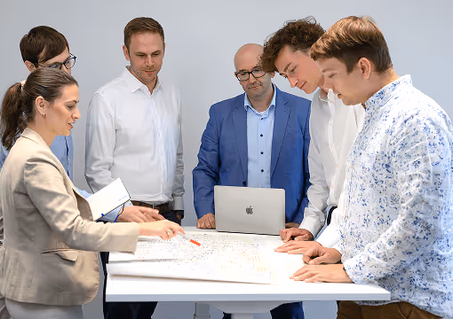 Sechs Personen diskutieren um einen Tisch, konzentrieren sich auf Pläne und Notizen. Büroatmosphäre, Zusammenarbeit.