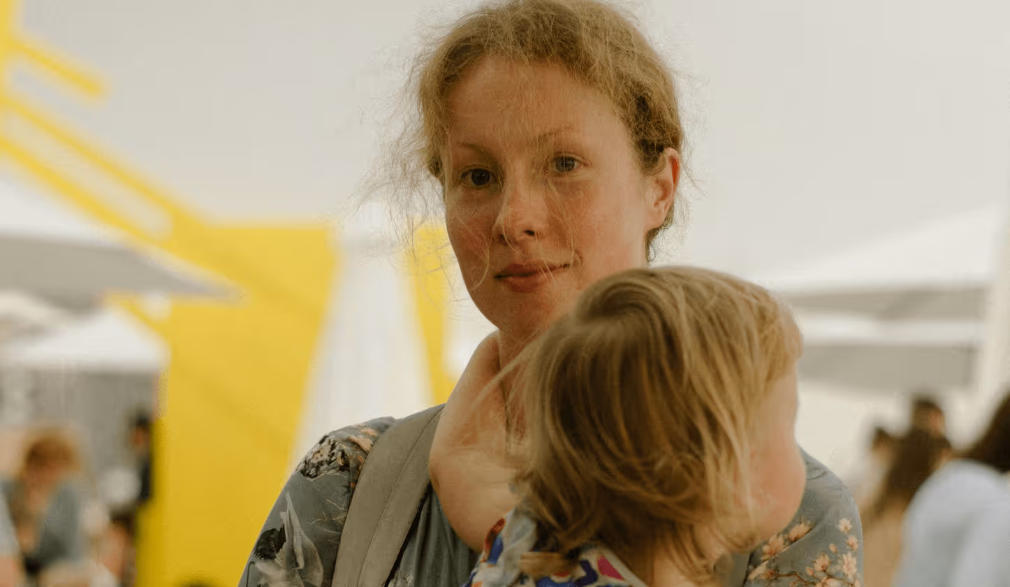 Frau mit Kind im Arm, gelbes Hintergrunddetail, lächelnd, entspanntes Sommerambiente.