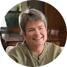 Lachende Person in grünem Hemd im Innenraum mit Holzmöbeln im Hintergrund.