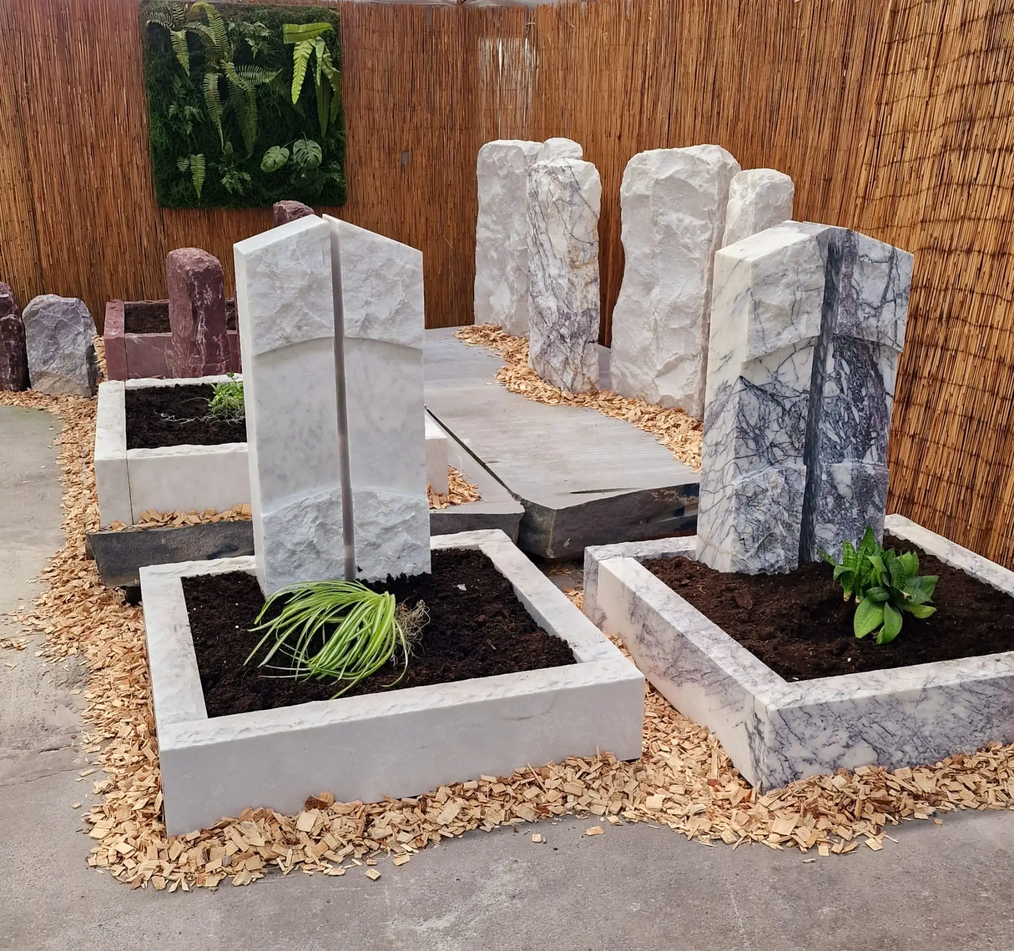 Grabsteine aus Marmor mit Pflanzen in einem Ausstellungsraum mit Bambuswänden.