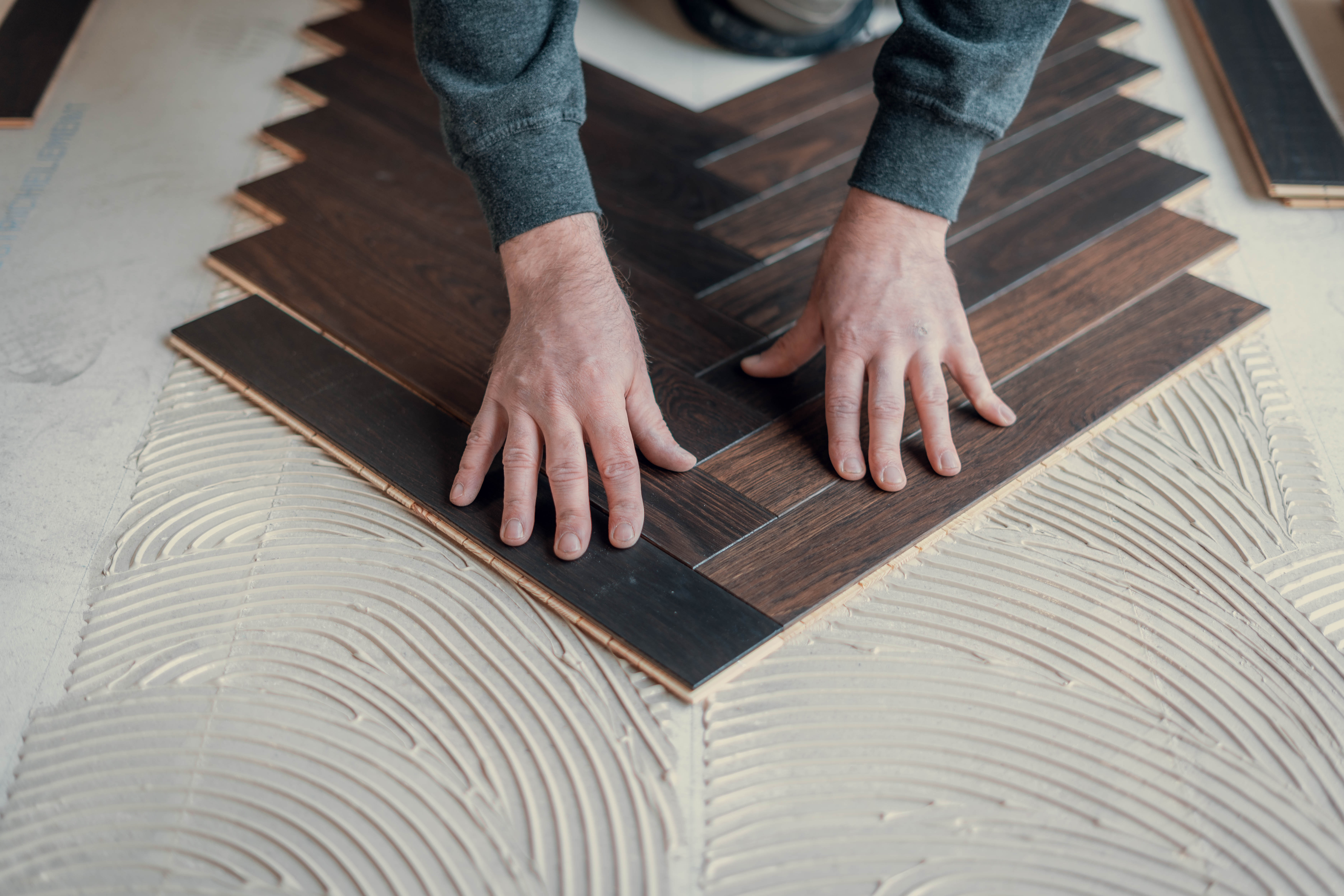 in Parkettleger von Hauptstadt Parkettleger verlegt präzise dunkles Fischgrät-Parkett auf einen vorbereiteten Klebeuntergrund.