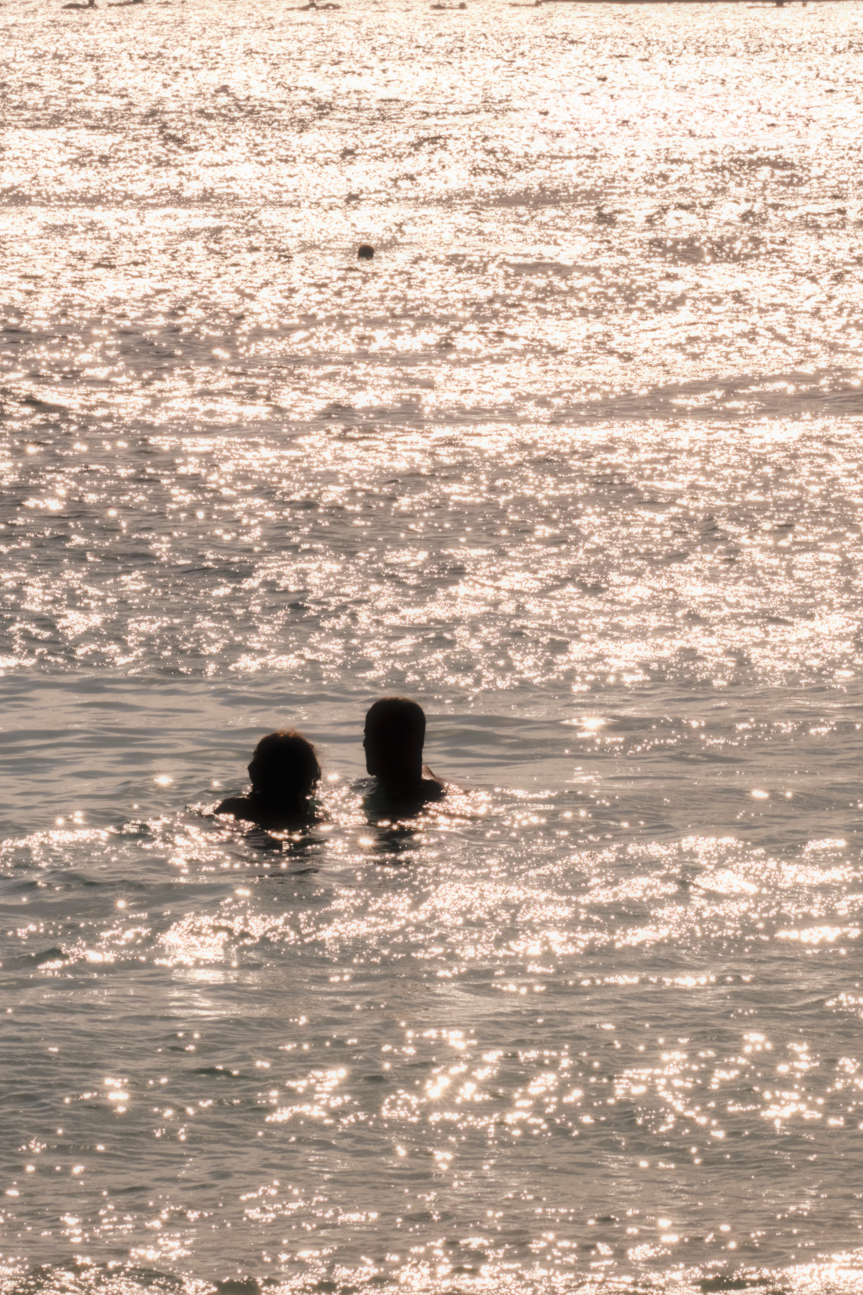 Two people swimming in the sea with sunlight sparkling on the water surface.
