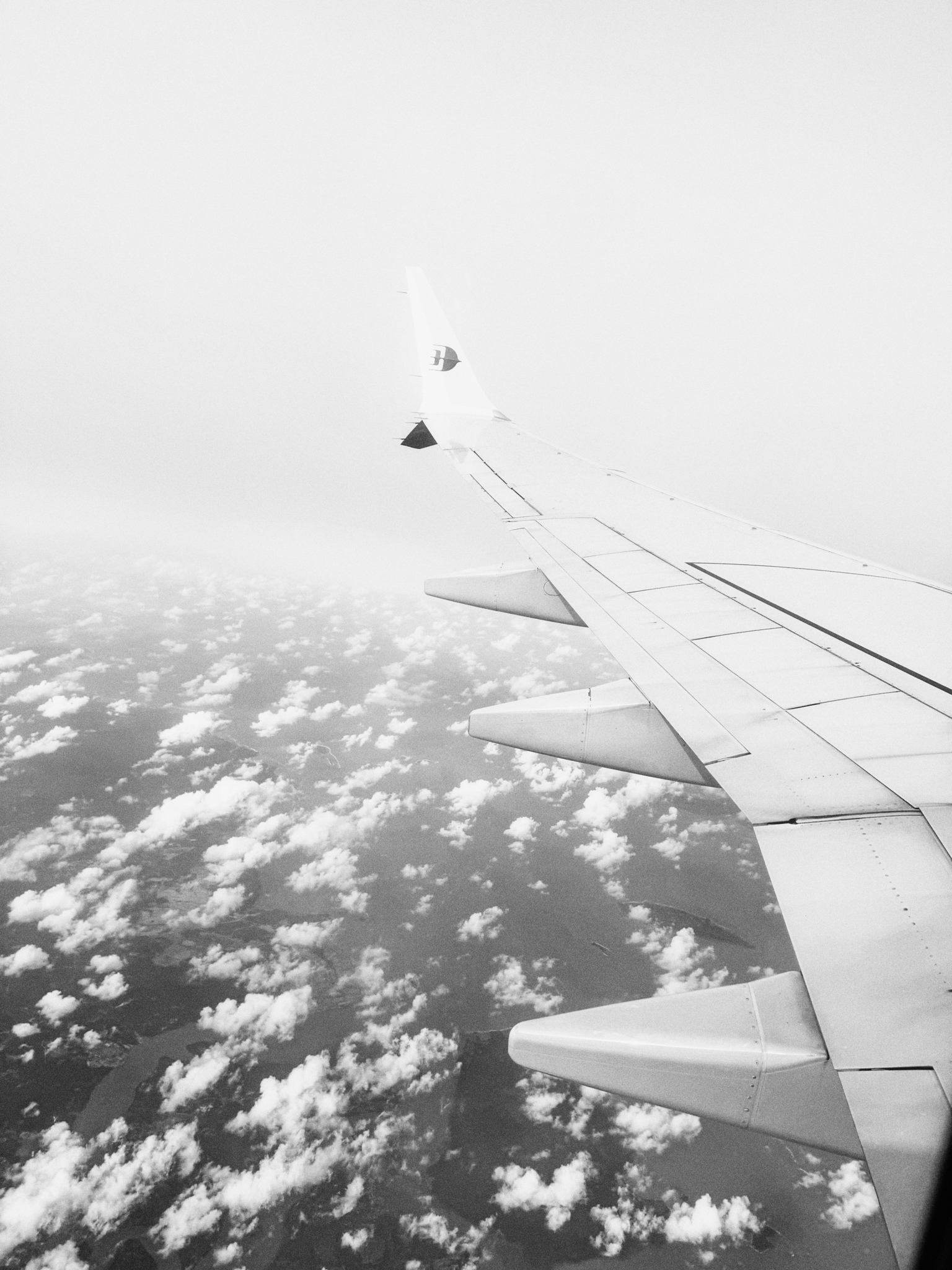 View of an airplane wing above scattered clouds and land seen from the window.
