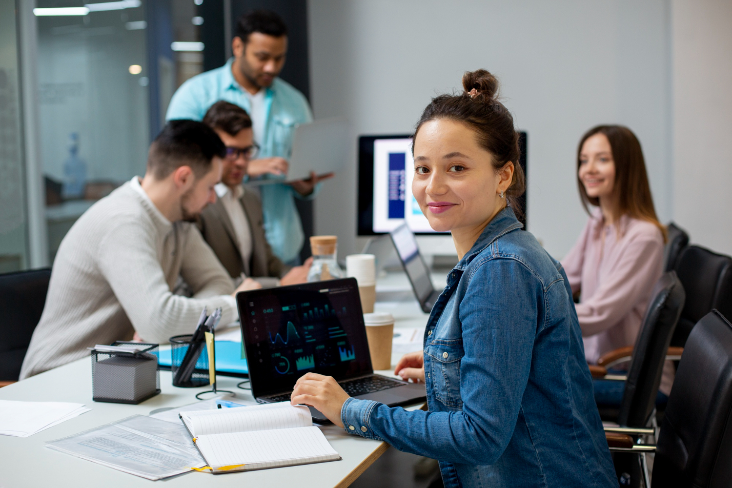 a woman sitting at a table with a laptop and people behind her