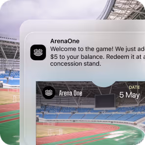Notification on a device screen from ArenaOne about adding $5 to balance redeemable at a concession stand, with a stadium track and seating in the background.