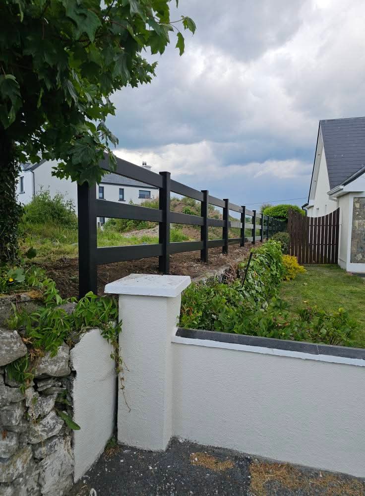 Newly installed wooden post and rail fence alongside a gravel path with gardening tools and a white van in the background.
