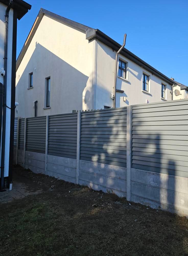 Light-colored wooden garden fence panel with lattice top placed on a stone patio next to a coiled green garden hose and a measuring tape.