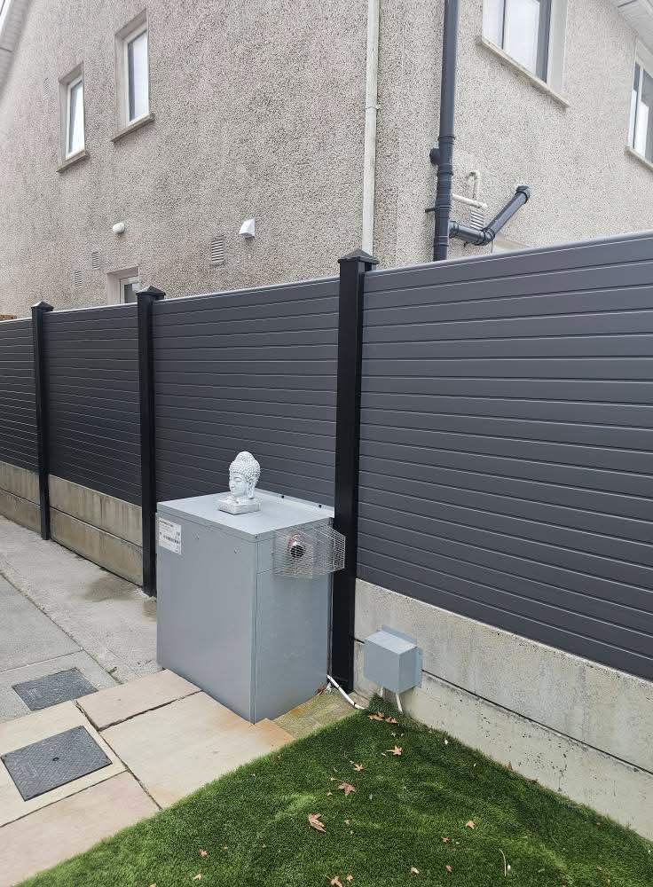 Section of newly installed wooden board fencing with concrete posts and base panels, next to a workbench holding a power drill and box of screws on muddy ground.
