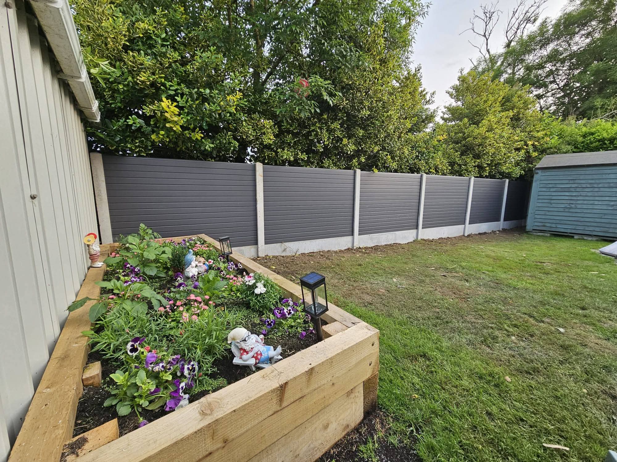 Backyard with green grass, a tiled patio, a wooden fence, and an exterior air conditioning unit mounted on a concrete slab.
