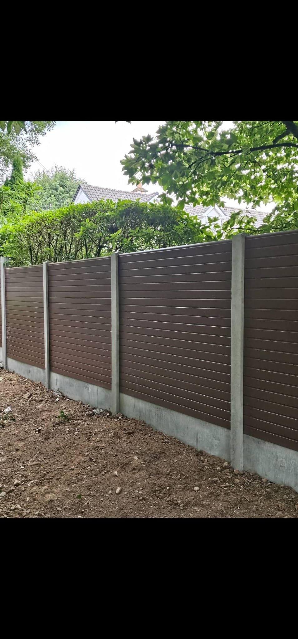 Light-colored wooden garden fence panel with lattice top placed on a stone patio next to a coiled green garden hose and a measuring tape.