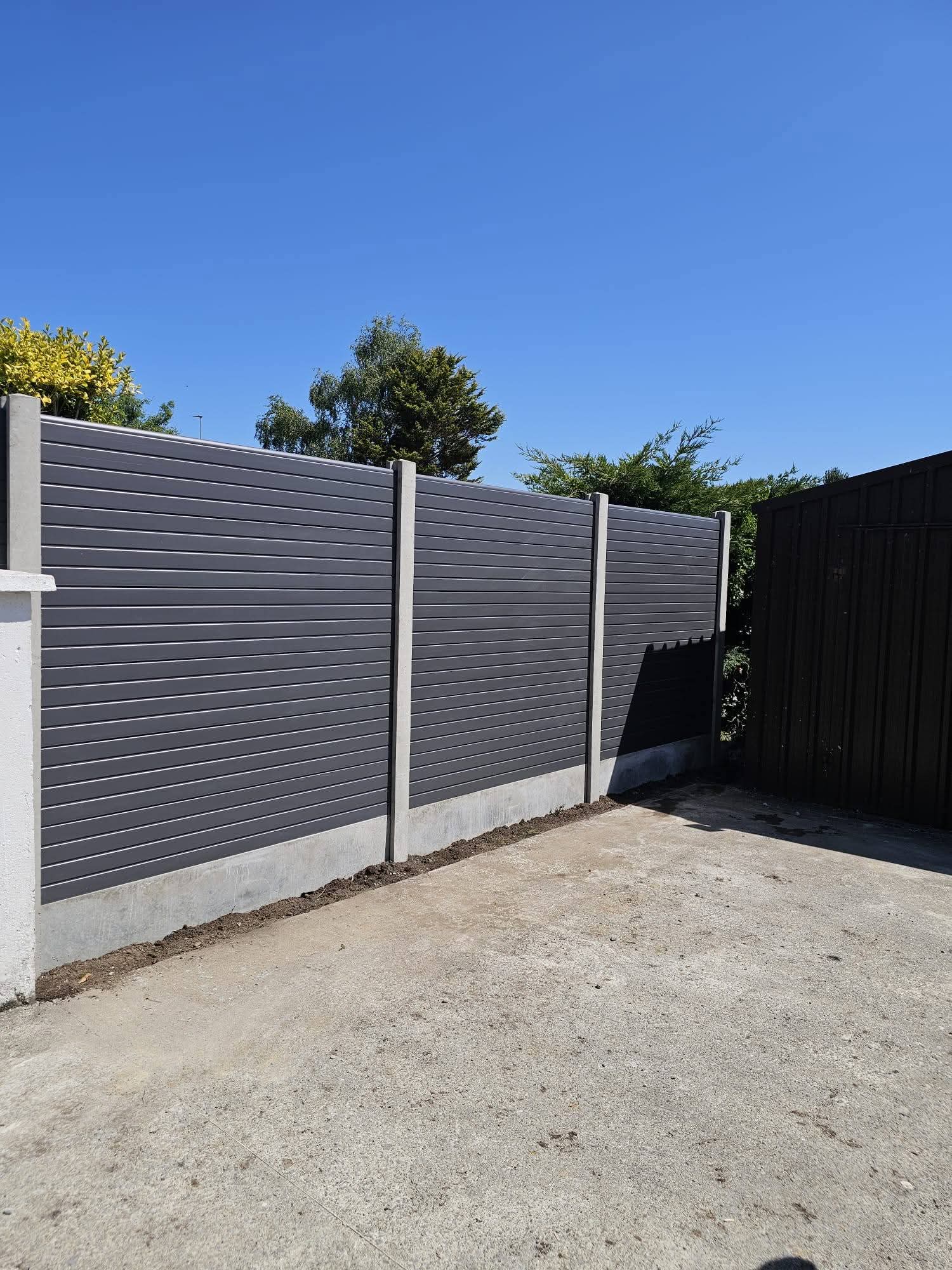 Light-colored wooden garden fence panel with lattice top placed on a stone patio next to a coiled green garden hose and a measuring tape.
